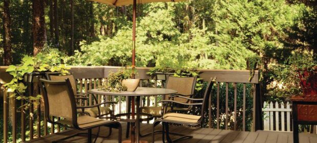 Wooden deck with four patio chairs around an umbrella-covered table with a forested background