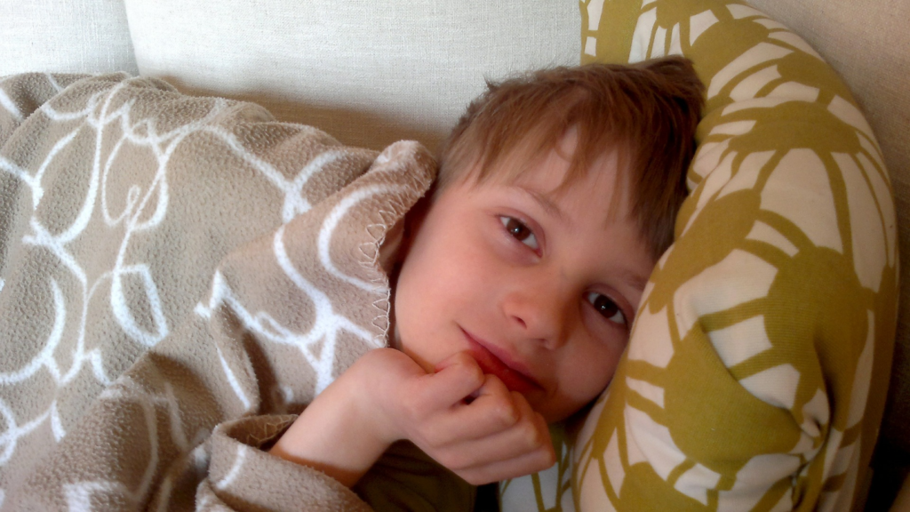 Child lying on couch under blanket smiling at camera