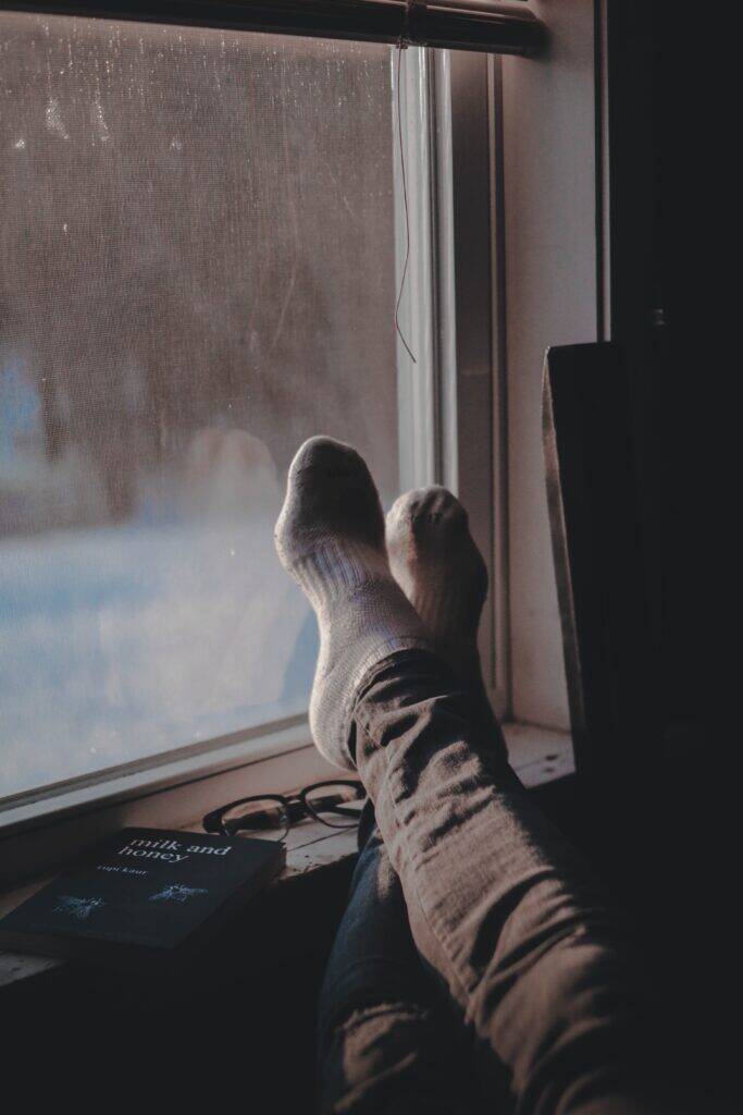 Person's besocked feet propped up on windowsill with snow outside