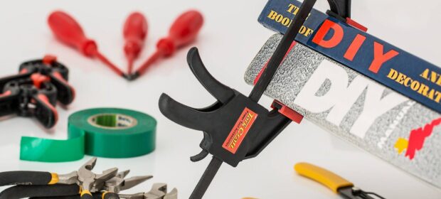 Clamp holding DIY books, pliers, and other tools on a white field