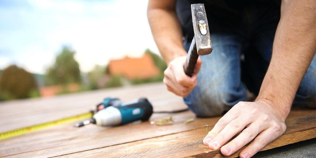 An image of a man hammering nails into a plank of wood.