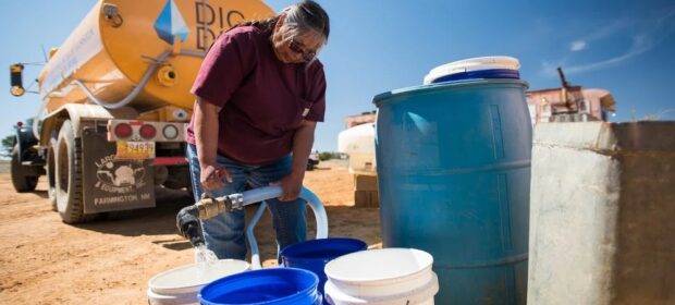 A woman filling water storage from a truck.